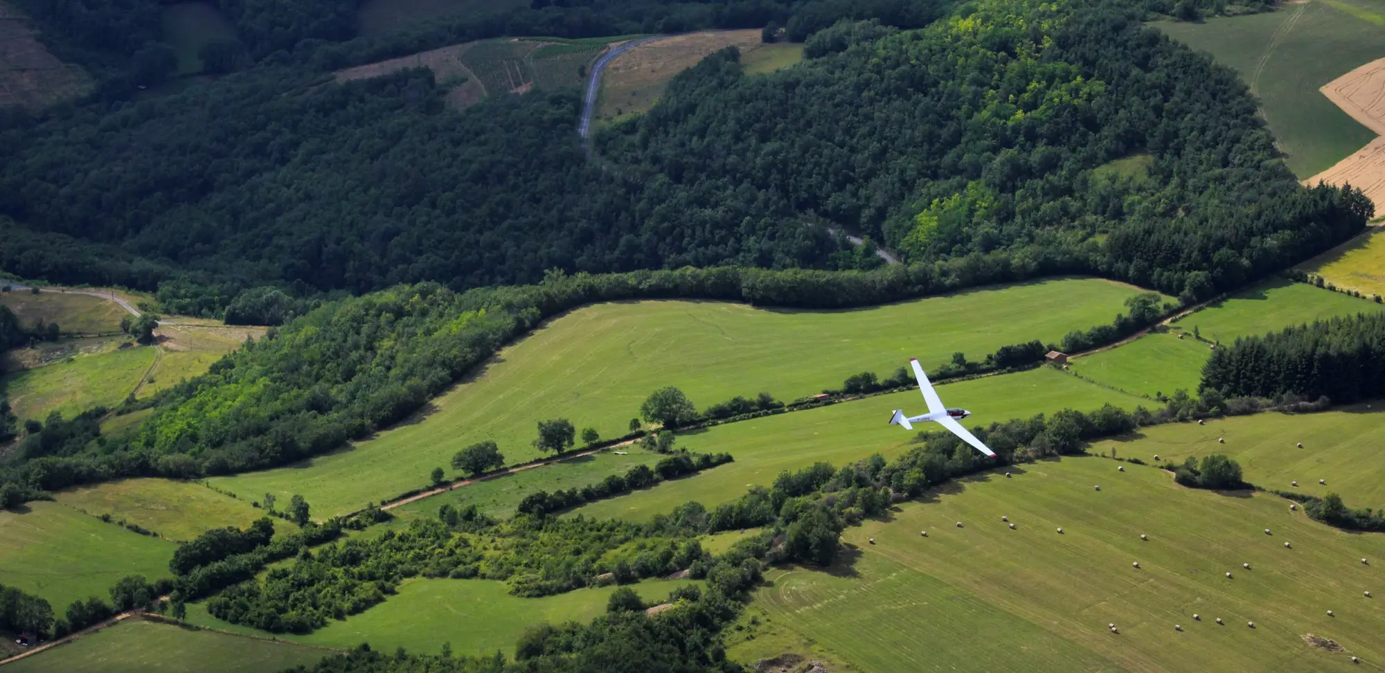 Un planeur blanc survole les prairies et les bois du Beaujolais